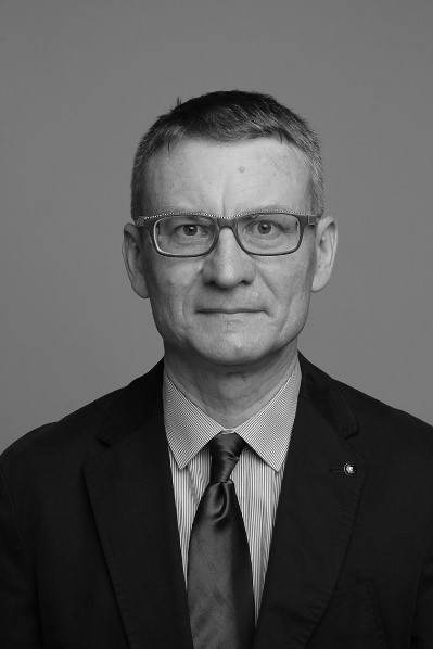 Portret artysty, fotografia czarno-biała. Mężczyzna w średnik wieku w okularach, patrzący wprost na widza, ubrany w czarna marynarkę, jasną koszule i ciemny krawat.