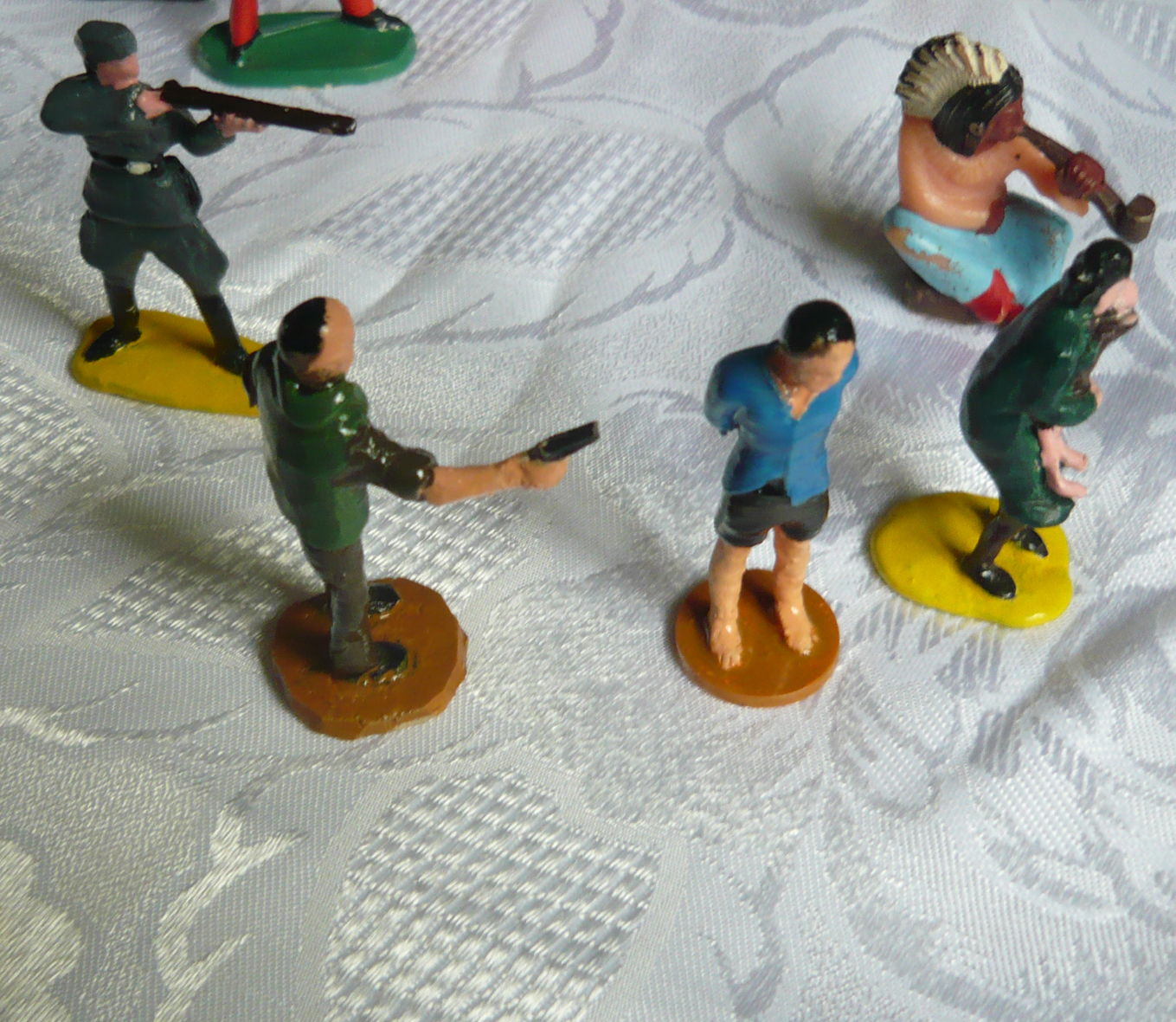 Na zdjęciu małe figurki ludzi. dwie z nich trzyma broń i kieruje w kierunku pozostałych trzech.