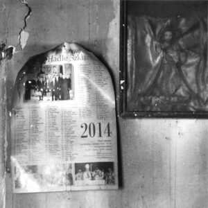 Czarno-biała fotografia przedstawia fragment gazety z 2014 roku, która układa się w prostokąt u góry zakończony półokregiem. po prawej stronie w styku z narożnikiem widnieje ikona.